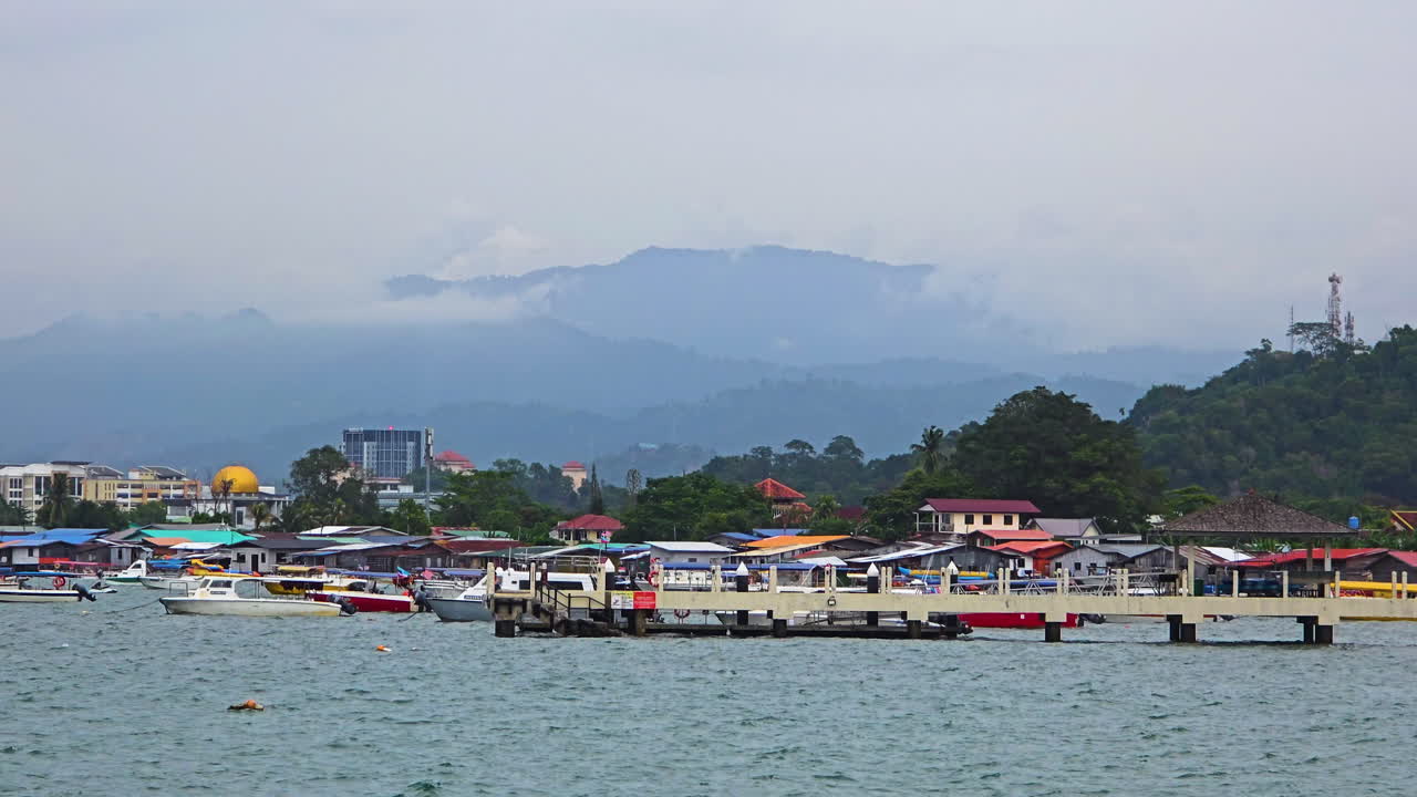 Tanjung Aru In Kota Kinabalu - Vibrant Houses And Boats At The Jetty With Misty Hills In Background. wide, zoom-in shot