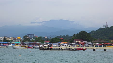 tanjung aru in kota kinabalu - vibrant houses and boats at the jetty with misty hills in background. wide, zoom-in shot
