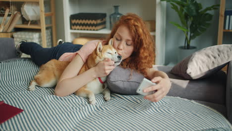 girl kissing her shiba inu dog while taking a selfie.