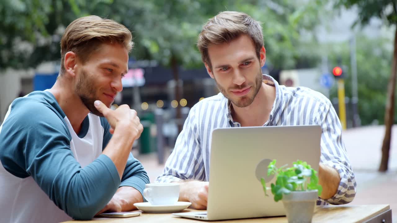 Friends discussing over laptop while having coffee in caf&Atilde;&copy; 4k