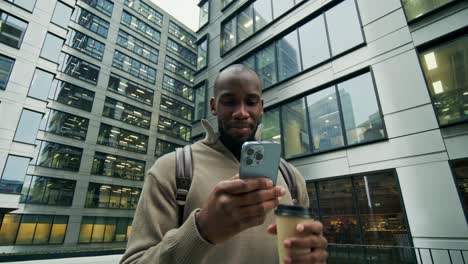 man using smartphone and drinking coffee outside office buildings