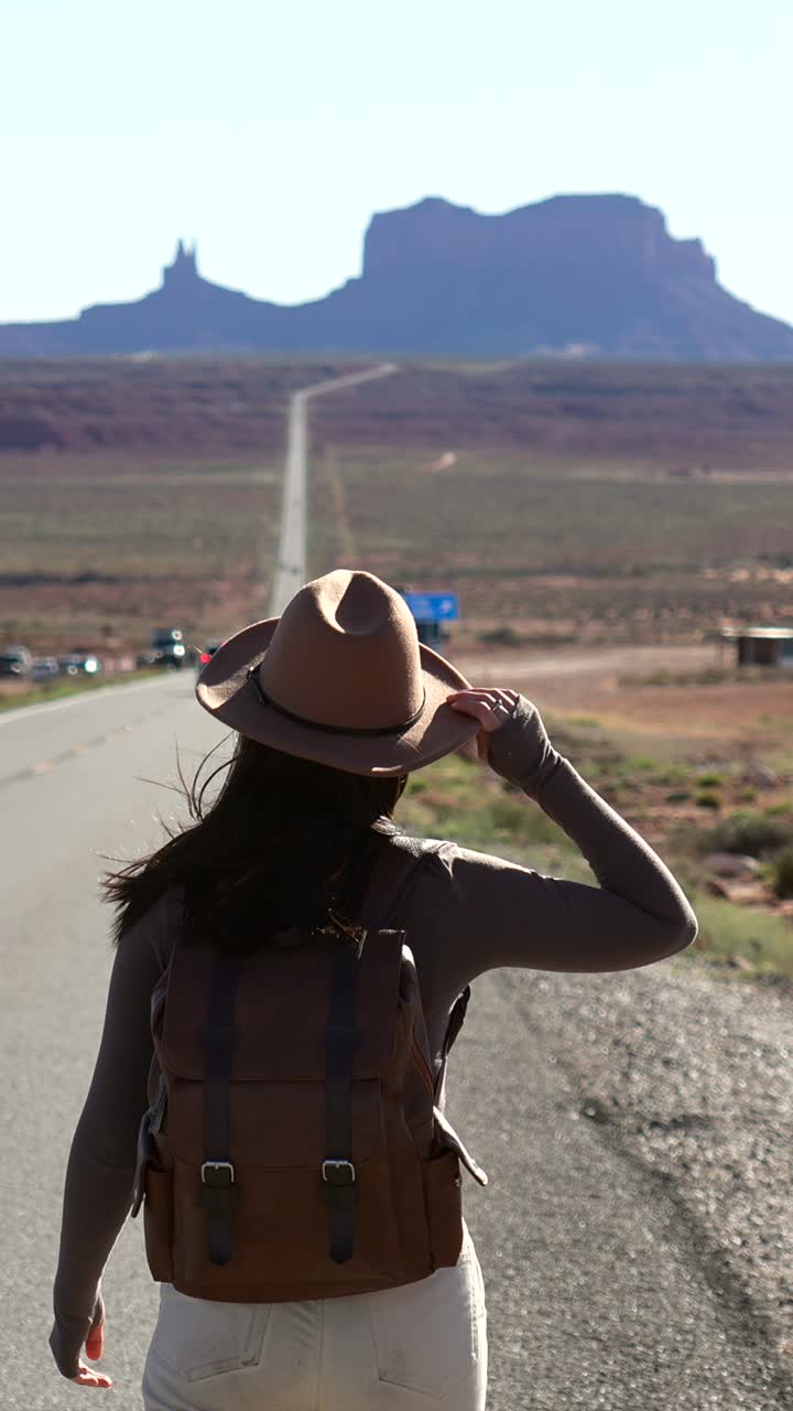 Donna con cappello e zaino che cammina su una strada desertica