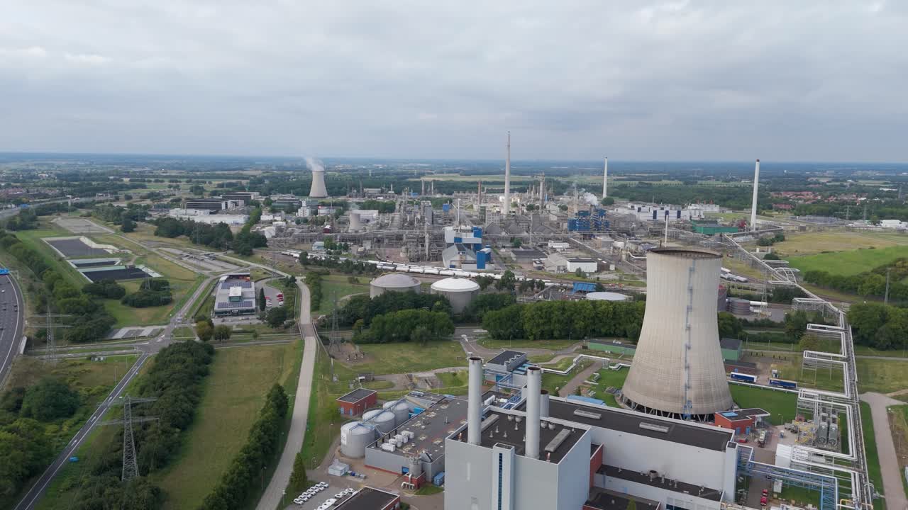 Wide drone footage of an industrial factory complex with smokestacks, cooling tower, and surrounding roads in the Netherlands