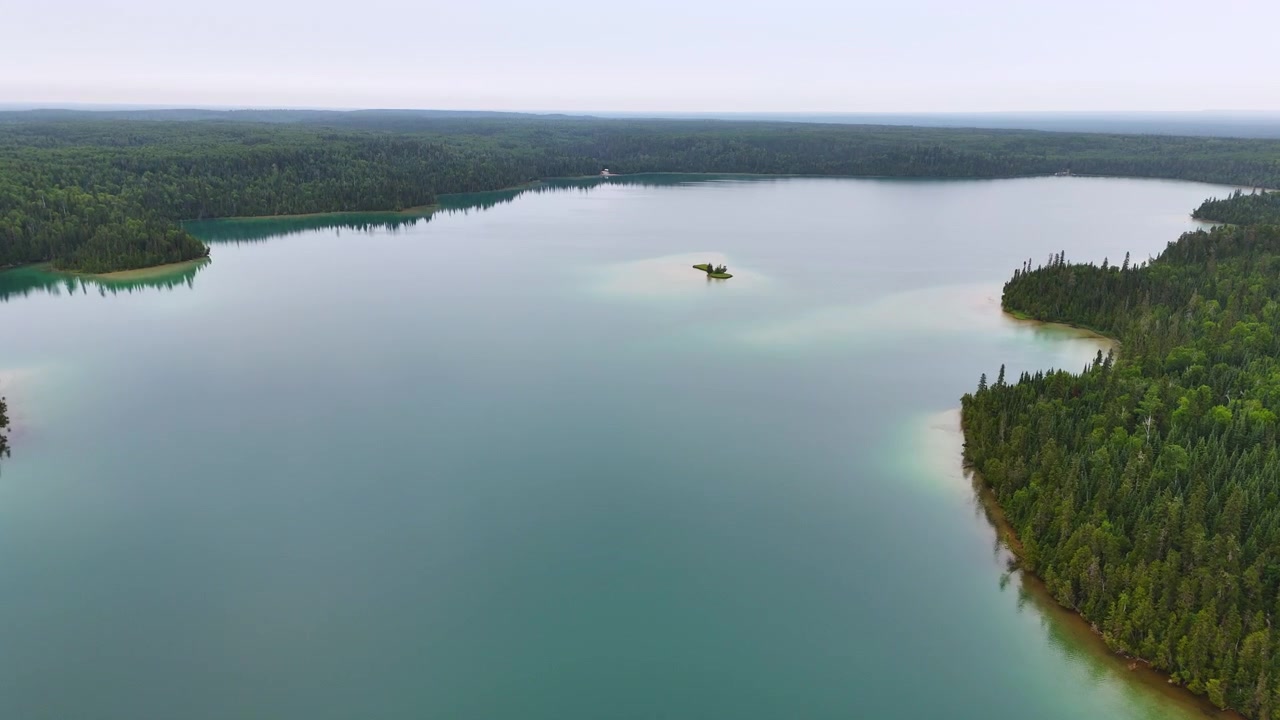 Vista aérea de águas calmas e turquesa refletindo um céu nublado, cercado por densa floresta boreal no Lago Big Skunk, no Norte de Ontário.