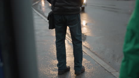 close view of two individuals waiting by the roadside, with a white bus approaching and a red truck following