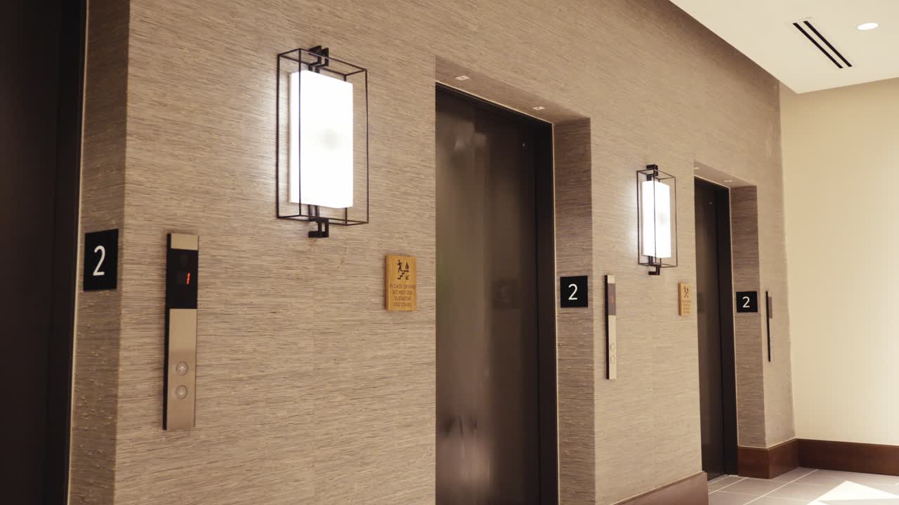 Symmetrical perspective of a luxury hotel elevator hallway featuring black and white tiled floors and minimalist wall sconces