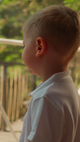 child stands near glass wall with frame at glamping. little boy rests in deluxe camping with dome cabin. kid waits for promenade near window