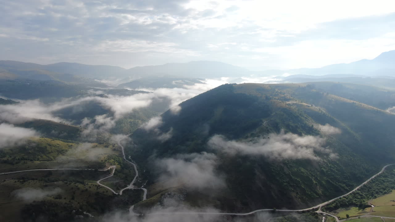 A view of mountains with fog filling the valleys A road winds through the landscape under a sky with light clouds