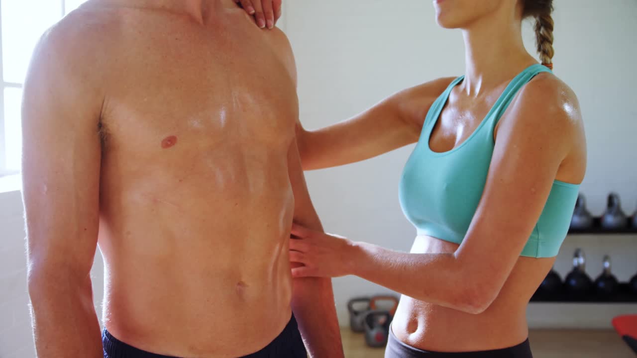 mujer sonriente tocando a un hombre musculoso en el gimnasio 4k
