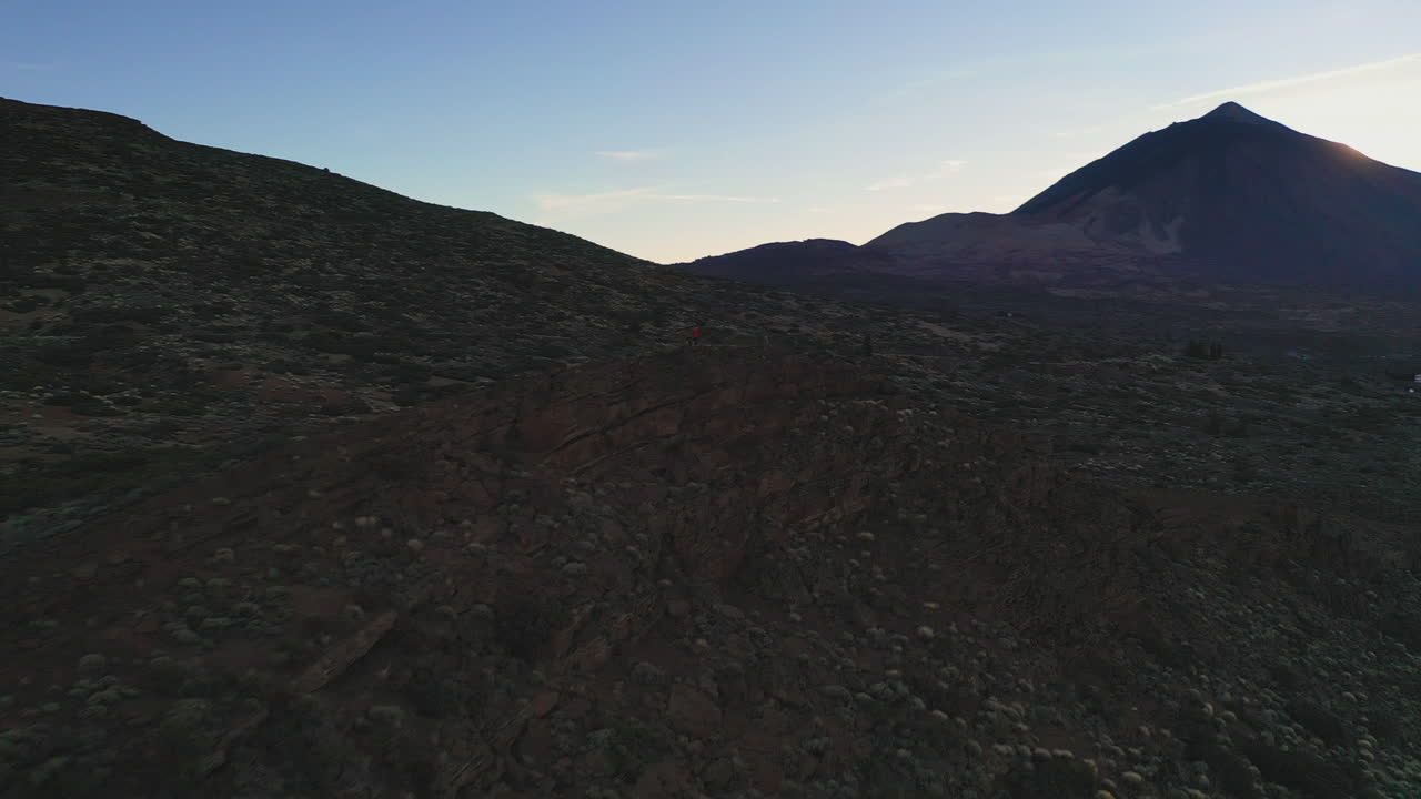 View of the cliffs and a rocky hillside below the Pico de Teide mountain on Canary Islands after sunset against a colorful evening sky. Cliffs and rocks below Pico de Teide in the evening 4K.