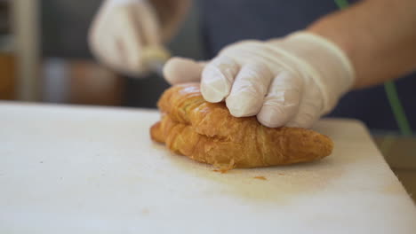 man hand cutting freshly baked croissant with long knife in bakery