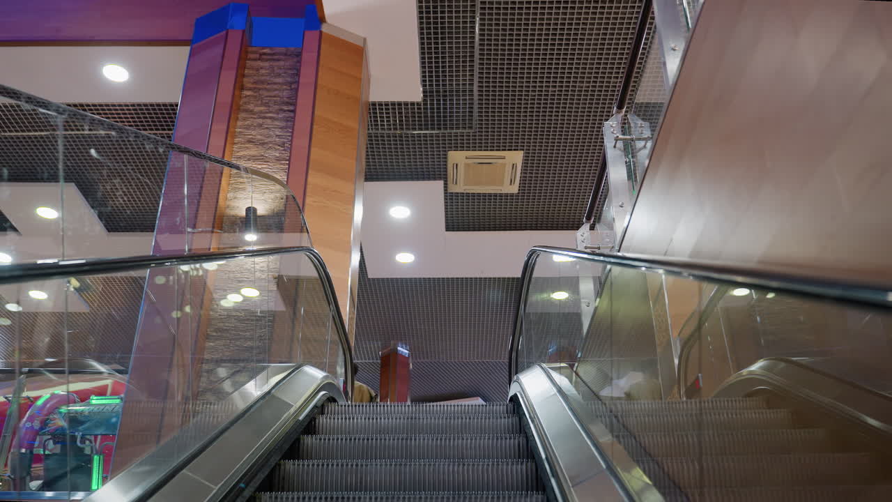 Man holding shopping bags steps out of escalator in modern mall interior with glass railing bright ceiling lights and retail atmosphere showing consumer lifestyle urban activity