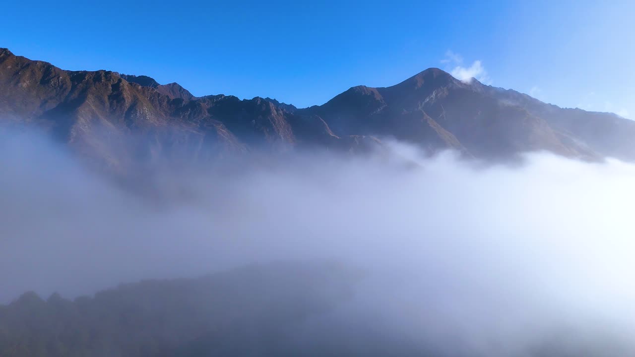A serene view of fog rolling over mountains at Moke Lake, Queenstown. Clear blue sky contrasts with the misty landscape