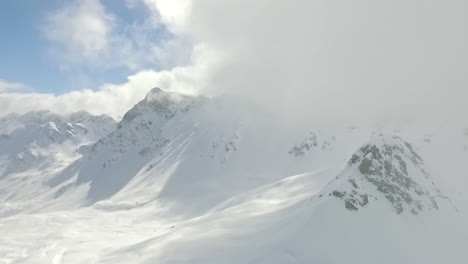 Aerial---Descending-shot-of-clouds-near-snow-covered-mountain-on-sunny-day