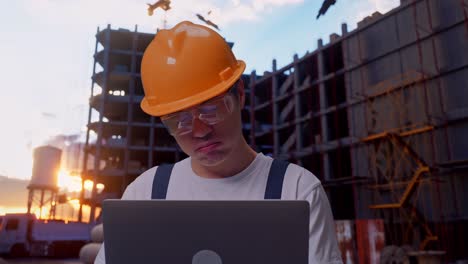 un trabajador asiático que usa una computadora portátil y tiene dolor de cabeza en el sitio de construcción