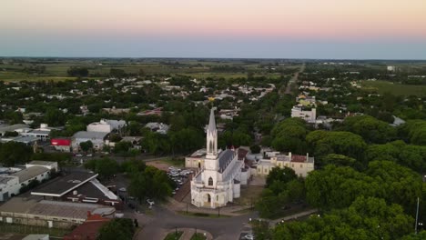 dolly fuera de la iglesia neogótica rodeada de árboles en la idílica ciudad rural de santa elisa al atardecer con fincas al fondo, entre rios, argentina