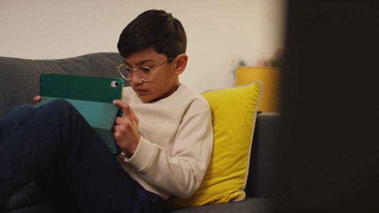 Primo piano di un bambino seduto sul divano di casa che gioca o guarda contenuti in streaming su un tablet digitale 9.