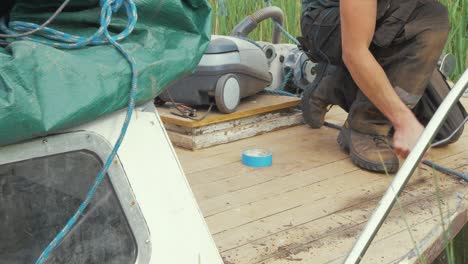 carpenter removes old caulking from boat foredeck using reefing hook