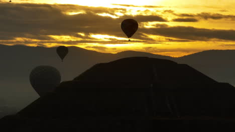 telephoto drone shot of a silhouette pyramid and hot air balloons, sunrise in mexico