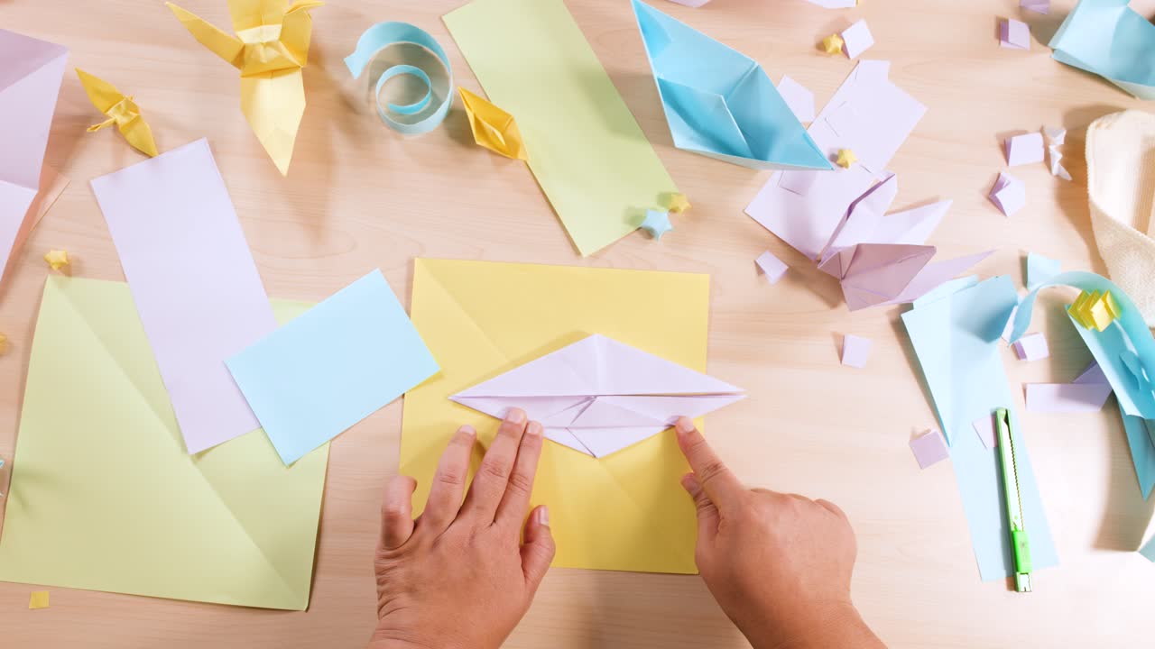 Vista dall’alto di mani che piegano con cura carta viola per creare origami su un’area di lavoro in legno