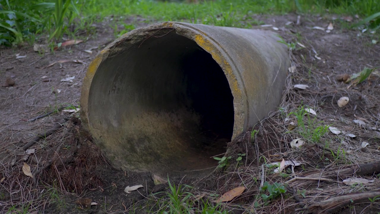 Primo piano in slow motion di un grande tubo di drenaggio cilindrico in cemento per fognature, adagiato nel terreno su una collina erbosa all'aperto vicino a una città suburbana della Central Coast, NSW, Australia