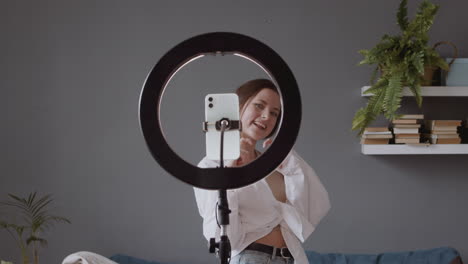 smiling young woman sending kisses and dancing in front of her smartphone camera to upload it to social media