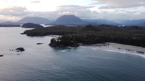 Ein-Hoch-Oben-Liegendes-Drohnenvideo-Eines-Wald--Und-Strandgebiets-Mit-Bergen-Und-Wolken-Im-Hintergrund-Bei-Sonnenuntergang