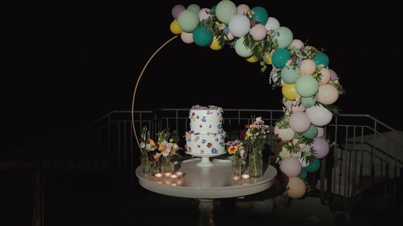 Mesa de tarta de boda decorada con flores, globos y velas por la noche