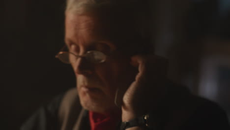 older passionate man evaluates an old watch in his office at night