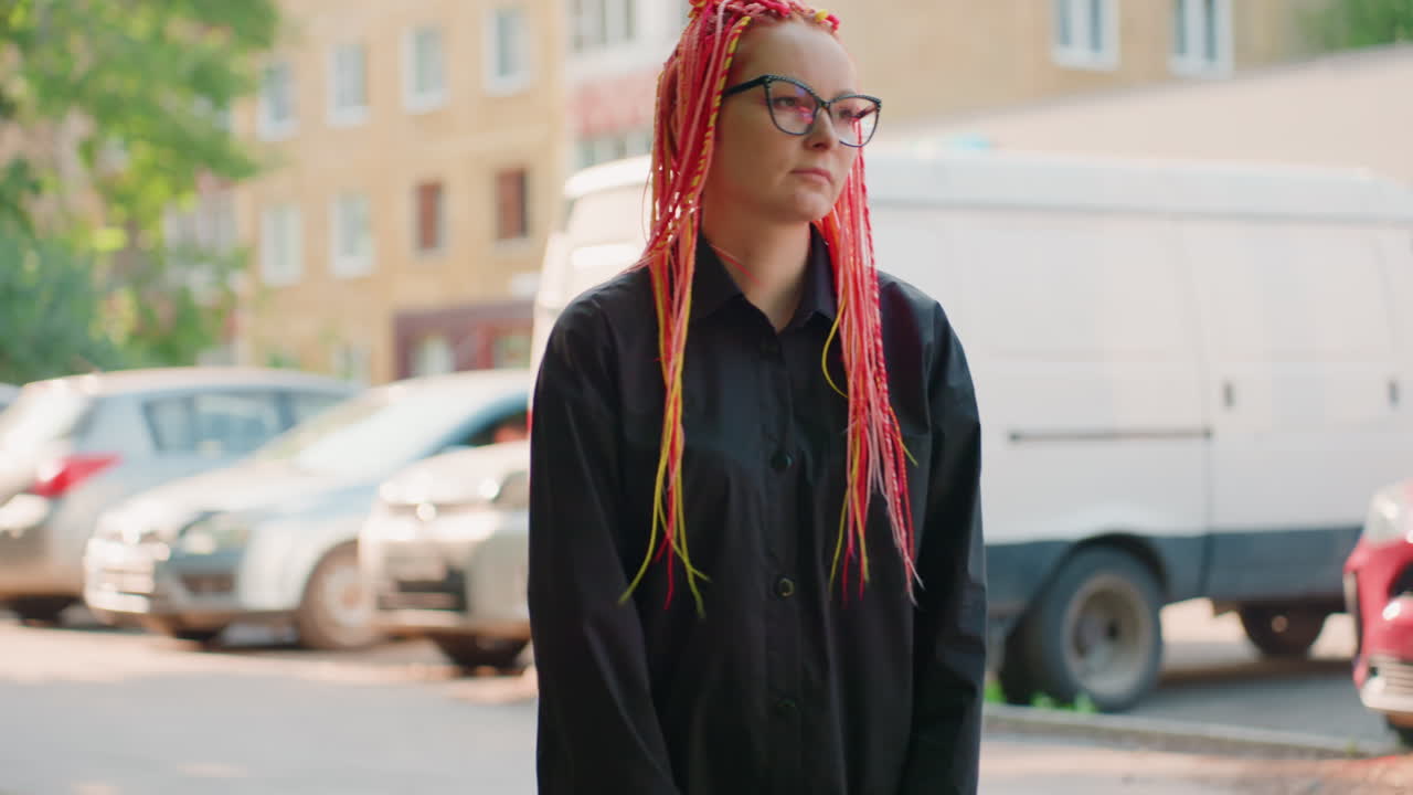 화려한 드레드락을 한 여성이 낮 동안 주차된 차에 기대어 있는 도시 풍경. 활기찬 분홍색 땋은 머리를 한 여성이 한낮 휴식 시간에 정차된 차량에 기대어 있어요.