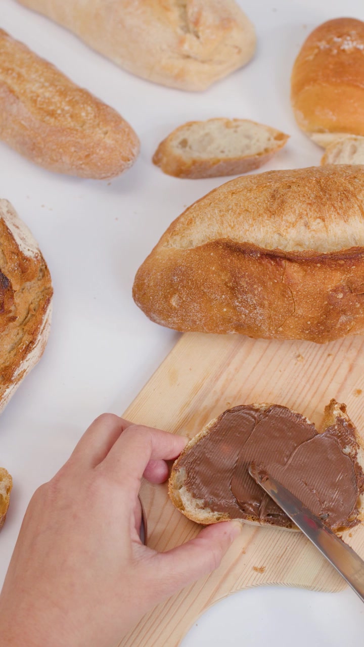 Close-up overhead shot of spreading chocolate cream on bread over a white background.