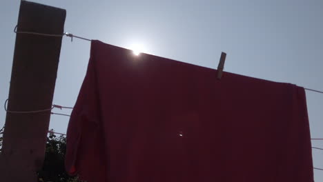 Sun-flare-on-pink-laundry-on-a-clothesline-in-backlight,-vertical-up-dolly-shot-in-slow-motion