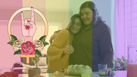 Animation-of-rainbow-flag-and-hand-with-roses-over-lesbian-couple-embracing-at-home