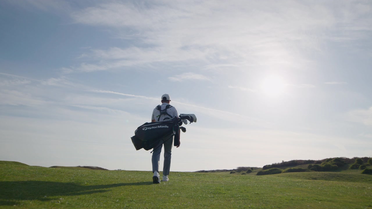 Ripresa al rallentatore da angolazione bassa di un golfista che cammina sul campo da golf