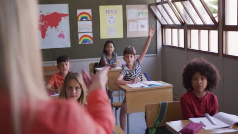 boy raising his hand while sitting on his desk at school