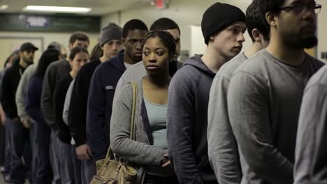 a diverse group of young adults waits in line, each individual expressing unique emotions while standing in a shared experience, captured in a city setting