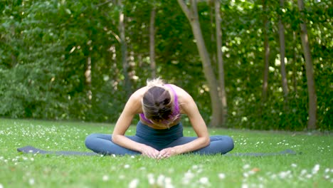 wide view of woman in athletic apparel stretching and exercising in a park as a gentle breeze blows her hair and small flowers in foreground