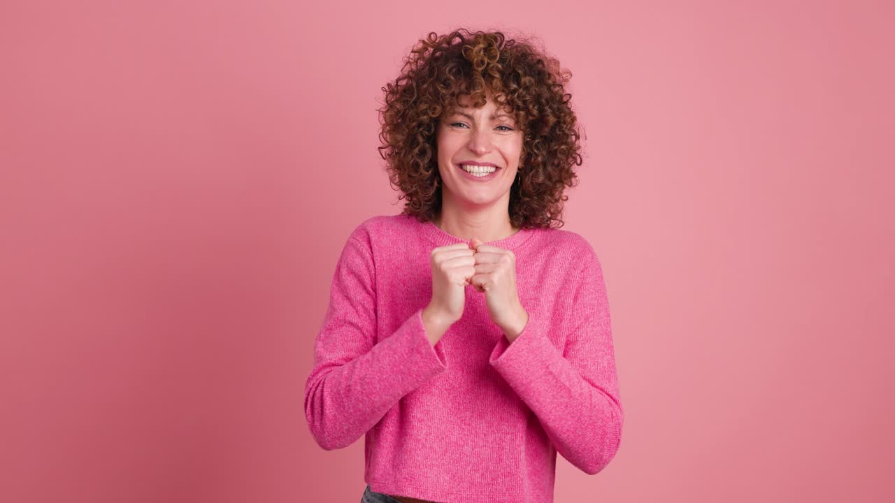 Excited young woman clapping hands and smiling on pink background