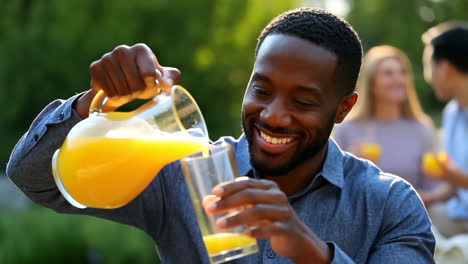 a smiling man pours orange juice into a glass at an outdoor gathering