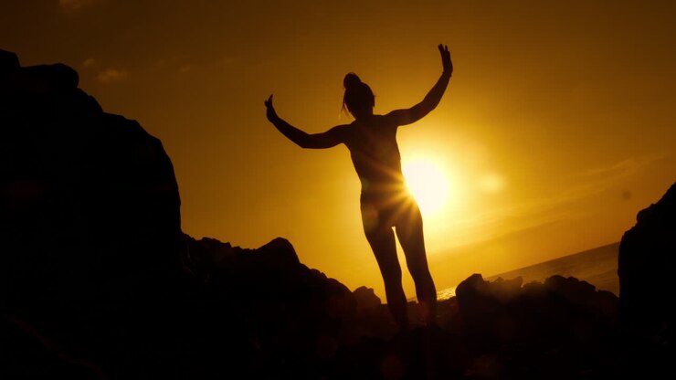 Woman Silhouetted at Sunrise/Sunset on Rocks by the Ocean