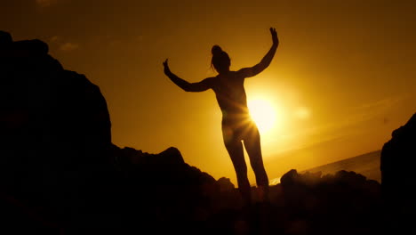 woman silhouetted at sunrise/sunset on rocks by the ocean