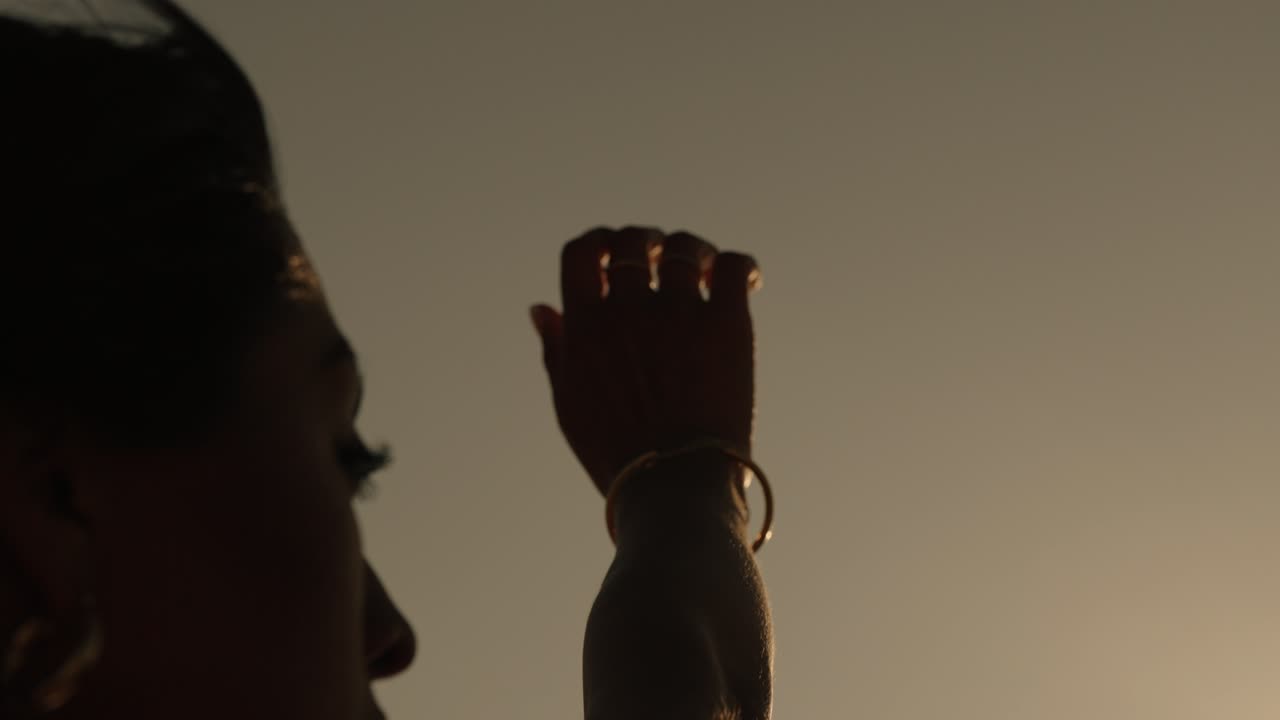 Close-up of a woman's face and raised hand in warm sunlight along the coast of Portugal, evoking softness and presence