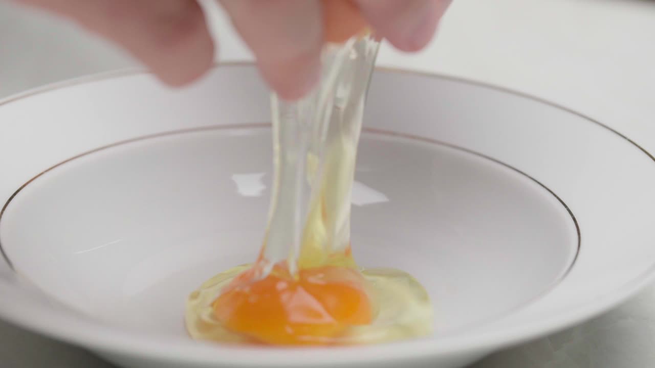 Mani che rompono un uovo crudo in un piatto bianco fondo su una superficie pulita della cucina