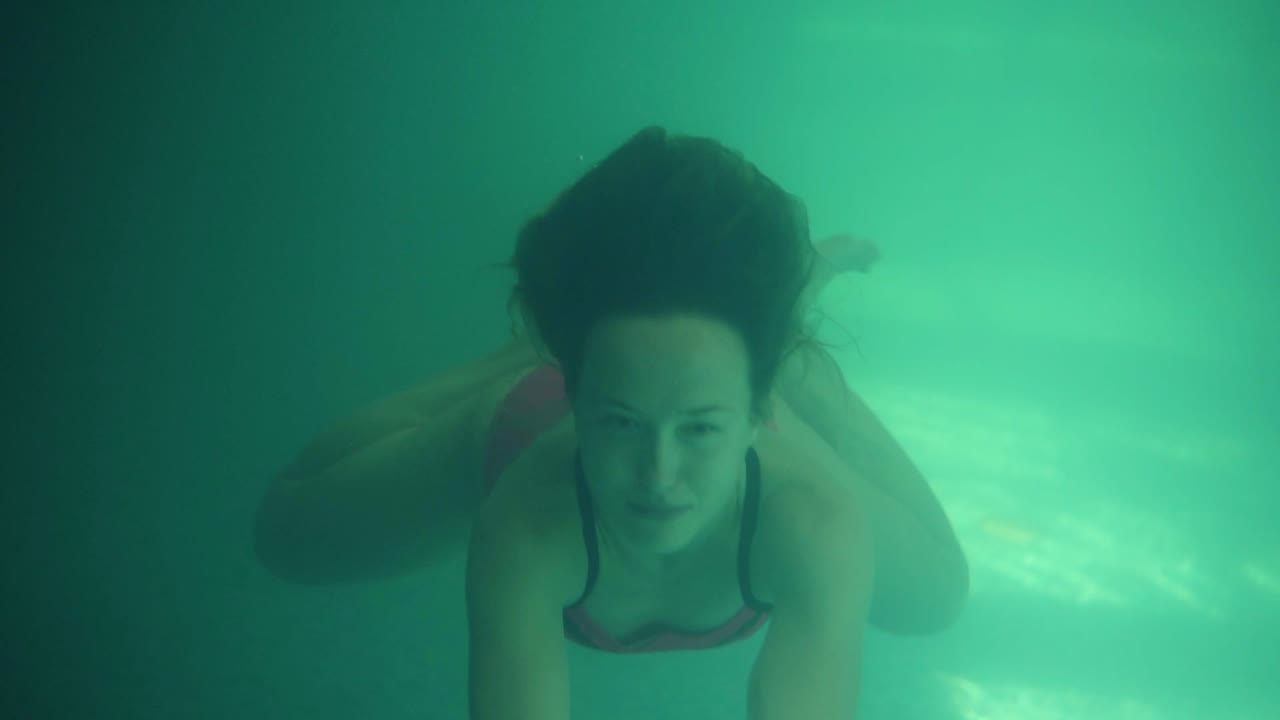hermosa mujer joven nadando en la piscina bajo el agua. hermosa vista frontal. agua azul y verde. sonriente