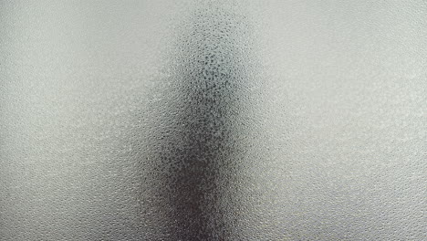 a female silhouette behind the frosted window touches the glass slowly