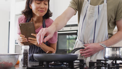 Video-of-happy-diverse-couple-preparing-meal-together-with-tablet