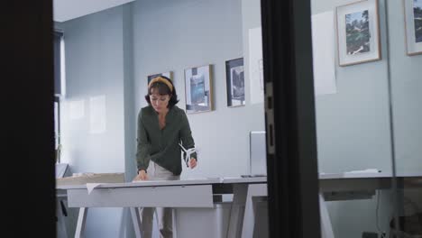 Biracial-businesswoman-standing-at-table-and-inspecting-model-alone-at-office