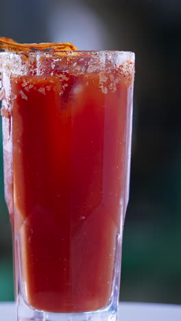red cocktails in a high glass with salt crystals on top. rotating beverage with a slice of dried orange on top. close up. blurred backdrop. vertical video