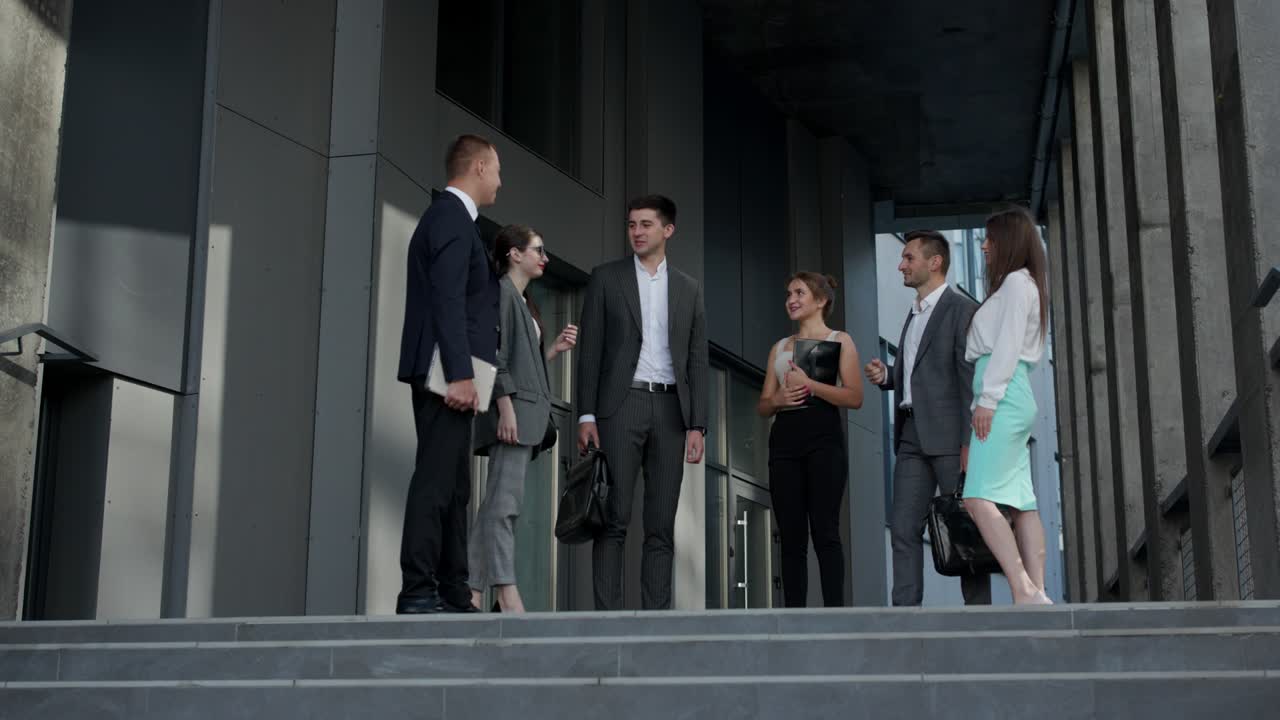 Business men and women in formal suits talk on the background of modern office building. Male and Female Business People Discuss Business. Group of six people