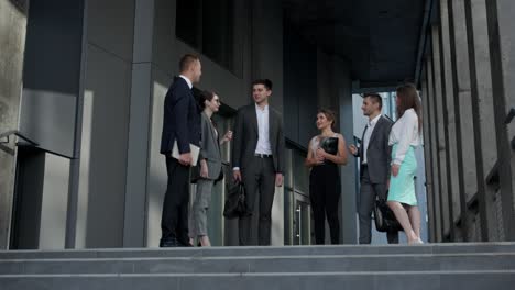 business men and women in formal suits talk on the background of modern office building. male and female business people discuss business. group of six people